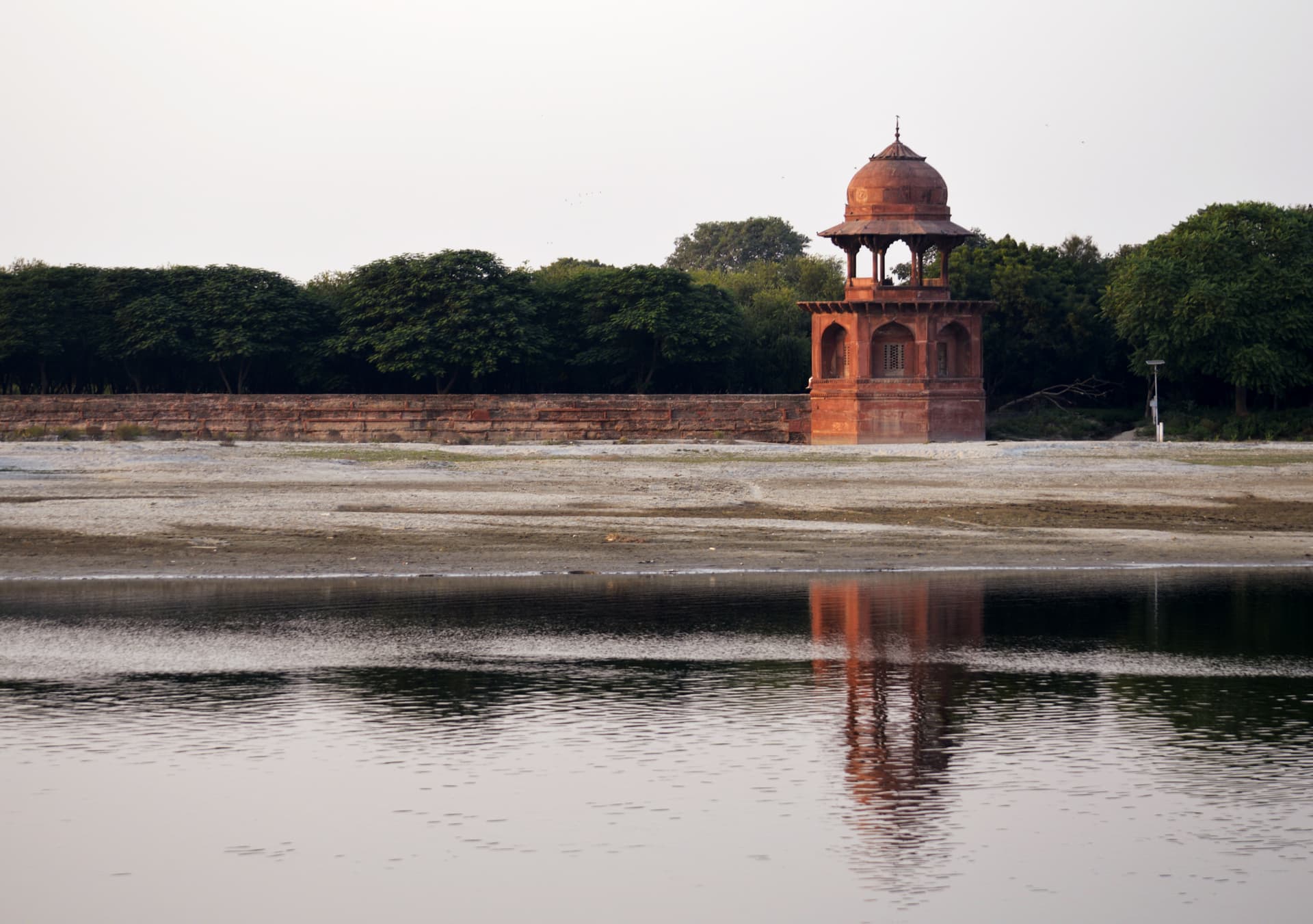 Mehtab Bagh corner pavilion, Agra — the surviving red sandstone tower of the Moonlight Garden, with the Taj Mahal visible across the Yamuna river.